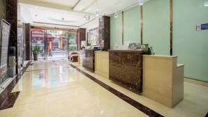 Zona de recepción de hotel con un mostrador de mármol, un área de estar y vistas a la calle.