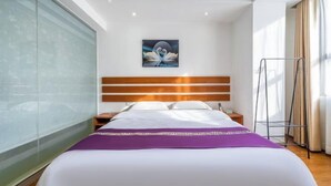 Habitación de hotel con cama, mesita de noche, un cuadro colgado en la pared y una ventana con cortinas.