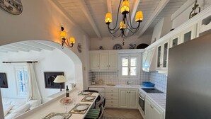 A kitchen with white cabinets, a black refrigerator, and a dining area with a table set for two. - Elia Oasis 2 Bd Magic Villa w Sea Views (Mykonos)