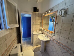 A bathroom with a toilet, sink, and mirror. There is a towel rack and a glass shelf with toiletries. - Elia Oasis 2 Bd Magic Villa w Sea Views (Mykonos)