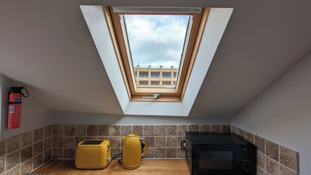 A small kitchen with a skylight, a toaster, a kettle, and a microwave. - Top Floor Apartment (Llandudno)