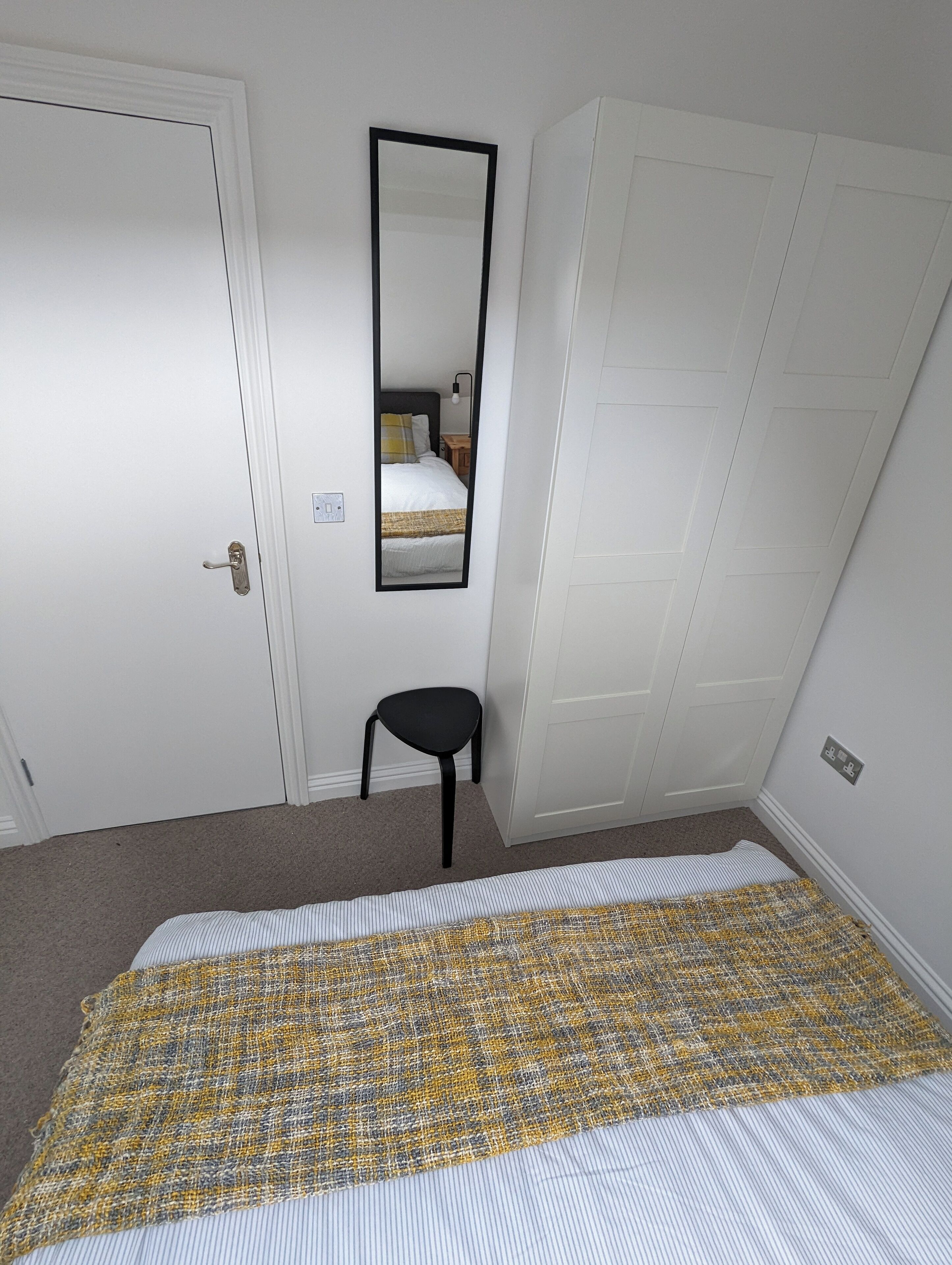 Un dormitorio con cama, una silla, un armario y un espejo.