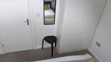 Un dormitorio con cama, una silla, un armario y un espejo.