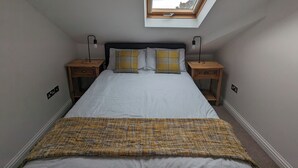 A bedroom with a skylight, a bed with striped bedding, two bedside tables with lamps, and a patterned throw blanket. - Top Floor Apartment (Llandudno)