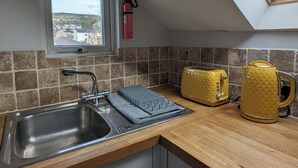 A kitchen with a modern design, featuring a stainless steel sink, wooden countertops, and a view through a skylight. - Top Floor Apartment (Llandudno)