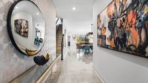 A hallway with a marble floor, a round mirror, and a large abstract painting on the wall.