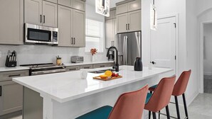 A modern kitchen with a central island, stainless steel appliances, and bar stools.