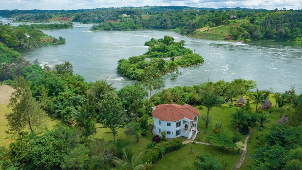 Une grande maison avec un toit rouge, entourée d’une végétation luxuriante et bordée par une rivière.