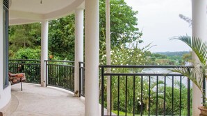 Un balcon abrité, doté d’une balustrade incurvée, de colonnes blanches et offrant une vue sur une végétation luxuriante et une rivière.