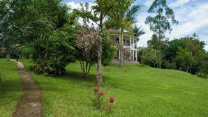 Un jardin luxuriant, avec un sentier menant à un bâtiment doté d’un toit recouvert de tuiles rouges et d’un balcon.