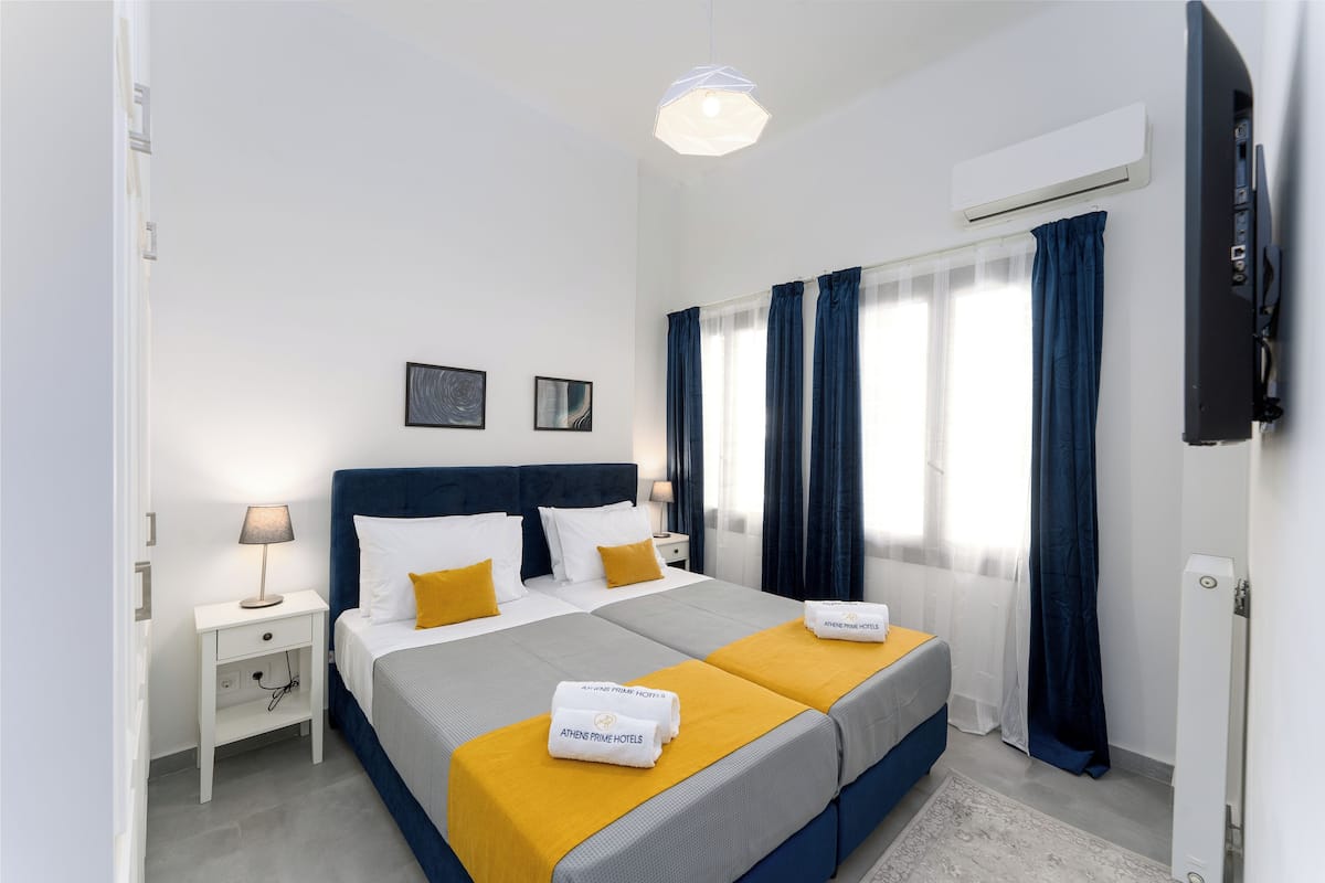 Una habitación de hotel con una cama grande, una mesita de noche, una lámpara, un equipo de aire acondicionado y un televisor.