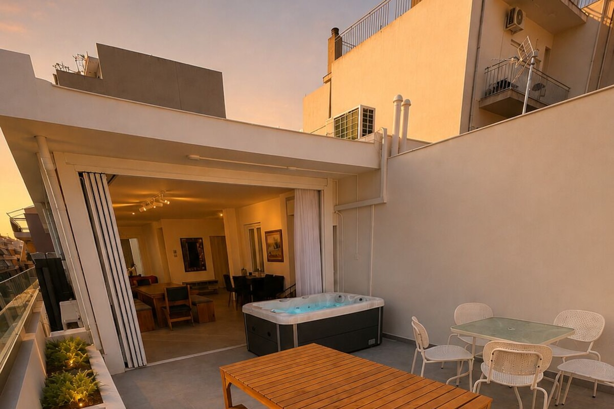 Un patio moderno al aire libre con una mesa y bancos de madera, rodeado de sillas blancas y un jacuzzi.