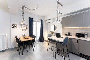 Une cuisine moderne équipée d’un four à micro-ondes, d’une machine à café et d’un ordinateur portable posé sur le comptoir. On y trouve également une table à manger avec des chaises et une horloge au mur.