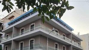 Un immeuble résidentiel à plusieurs étages, doté de balcons, d’un espace de stationnement avec des voitures et donnant sur la rue.