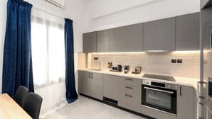 Une cuisine moderne avec des meubles gris, un four encastré et un plan de travail sur lequel se trouvent une machine à café et d’autres appareils électroménagers.