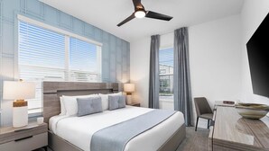 A modern hotel room with a large bed, two bedside tables with lamps, a desk with a chair, and a ceiling fan. - The Stylish | NEW Home w Designer Decor, PVT Pool & Theme BR - Mins to Universal (Orlando)