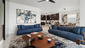 A modern living room with two blue sofas, a wooden coffee table, and abstract art on the walls. - The Stylish | NEW Home w Designer Decor, PVT Pool & Theme BR - Mins to Universal (Orlando)