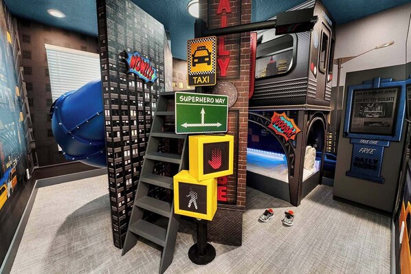 A room with a bed, a ladder, a sign for 'Superhero Way', and a 'Take One Free' sign.