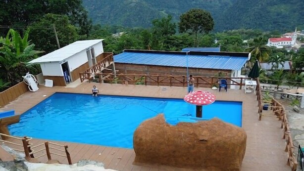 A swimming pool with a wooden deck, a small hut, and a thatched structure. - Balneario manantial  (San Pablo de Borbur)