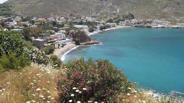 Un pueblo costero con edificios a lo largo de la costa, un telón de fondo montañoso y una vista despejada del mar.