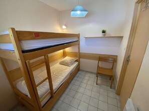Ein Schlafzimmer mit Etagenbetten, einem Schreibtisch und Stuhl, einem kleinen Regal mit einer Pflanze und einer Tür.
