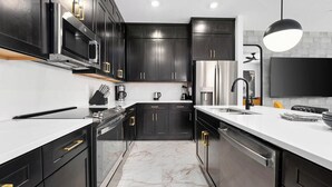 A modern kitchen with dark cabinetry, stainless steel appliances, and a marble floor. - Luke's Lookout | 5-Star Villa Near Disney w/ Grand LR, Kitchen, Dragon BR & Pool (Orlando)