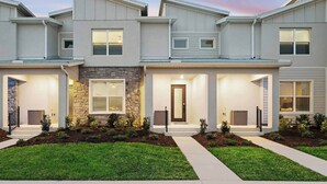 A modern townhouse with a stone accent wall, a front door, and a well-maintained lawn. - Luke's Lookout | 5-Star Villa Near Disney w/ Grand LR, Kitchen, Dragon BR & Pool (Orlando)