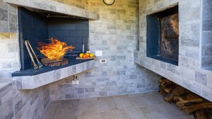 A stone-walled room with two fireplaces, one actively burning wood, and a small shelf with a picture frame and candles. - Villa Ambra by Villa Plus (San Vito dei Normanni)