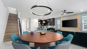 A modern dining area with a round table, teal chairs, and a ceiling light fixture.