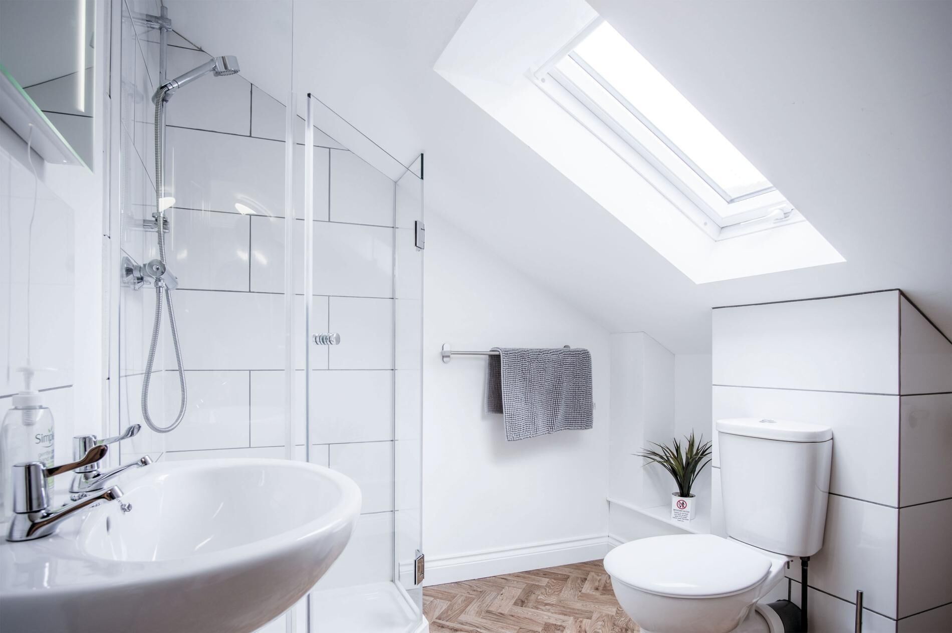 A modern bathroom with a skylight, a large sink, a shower, and a toilet.