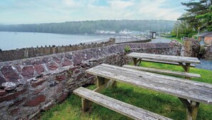Muro de piedra con zona verde y mesas de picnic con vista a un cuerpo de agua.