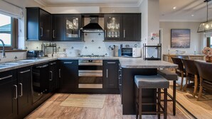 Une cuisine moderne avec des meubles de couleur sombre, un îlot central doté de tabourets de bar, des appareils en acier inoxydable et une vue sur l’espace repas.