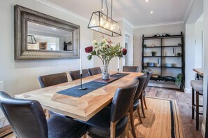 Un comedor con mesa de madera, sillas de cuero negro, un florero con flores y un espejo decorativo.