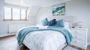 Une chambre à coucher avec un lit, une table de chevet, une lampe, un tableau et une fenêtre.