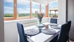 Un coin repas avec une table blanche, quatre chaises bleues et un vase de fleurs.
