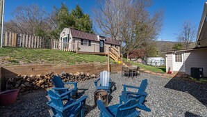 A backyard with Adirondack chairs, a fire pit, and a wooden deck leading to a house. - Stroll to Park, Shops, Restaurants in Downtown WJ! (West Jefferson)