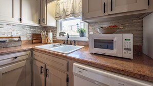 A kitchen with white cabinets, a granite countertop, a built-in microwave, and a window with curtains. - Stroll to Park, Shops, Restaurants in Downtown WJ! (West Jefferson)