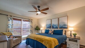 A bedroom with a bed, a ceiling fan, a nightstand, a lamp, and a window with curtains. - Stroll to Park, Shops, Restaurants in Downtown WJ! (West Jefferson)