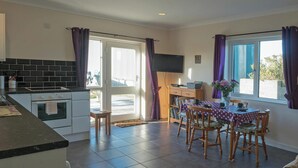 A kitchen with a dining area, a TV mounted on the wall, and a window with curtains. - Llainfawr Cottage Apartment, Fishguard (Letterston)