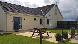 A single-story house with a tiled roof, a front door, and a picnic table in the yard. - Llainfawr Cottage Apartment, Fishguard (Letterston)
