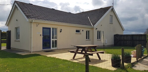 A single-story house with a tiled roof, a front door, and a picnic table in the yard.