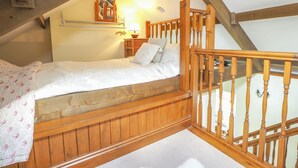 Un dormitorio acogedor en el ático con cama de madera, una mesita con lámpara y barandilla de madera.