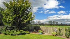 Patio trasero cercado con un gran árbol, césped y valla de madera.