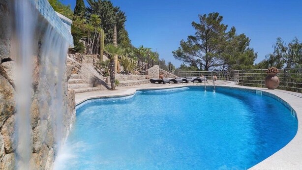 A swimming pool with a waterfall feature, surrounded by stone steps and palm trees.
