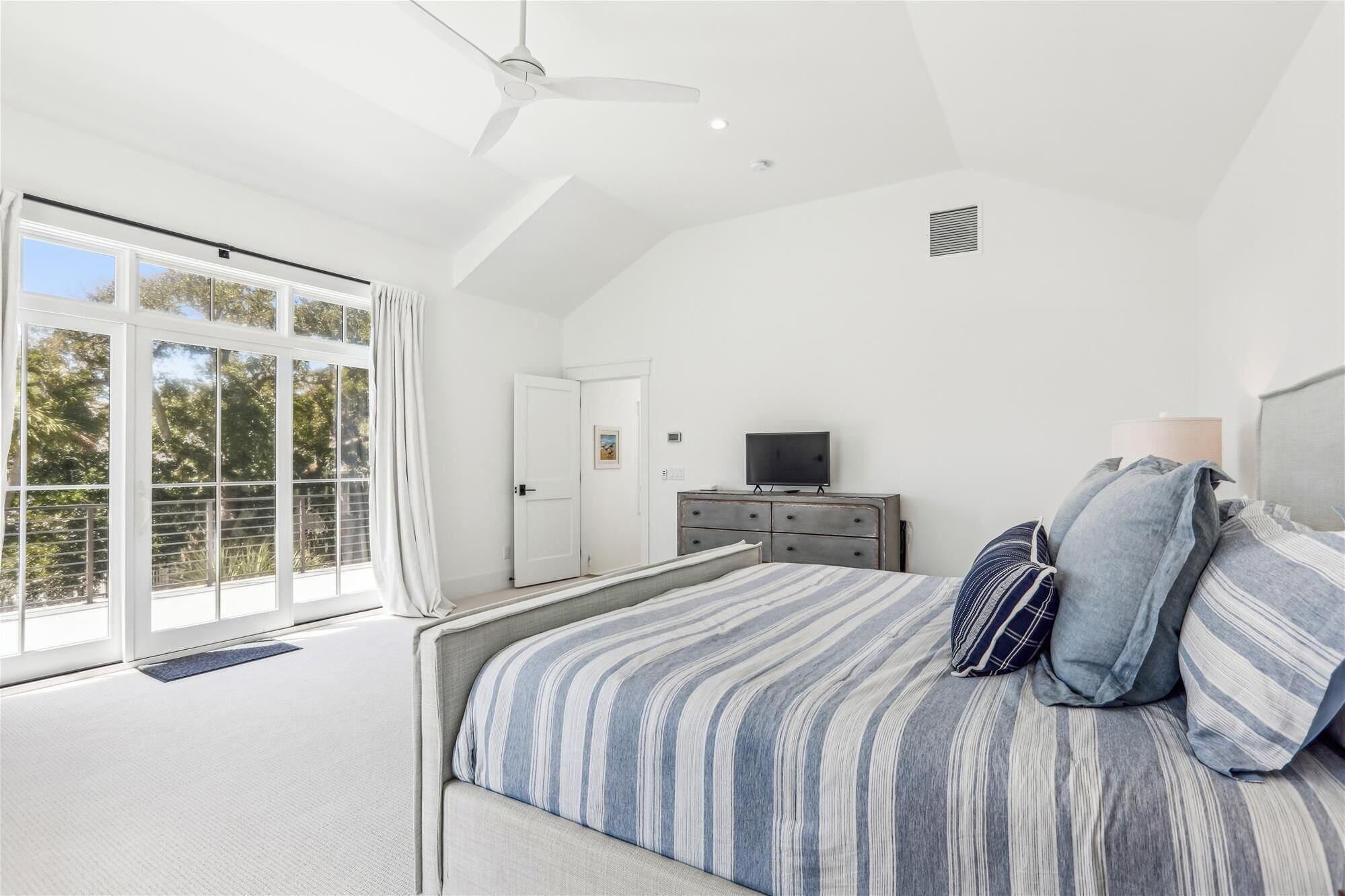 A bedroom with a large bed, a television, and a view of trees through the window.