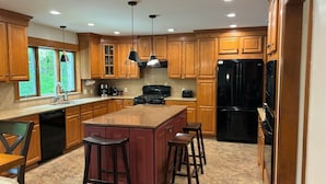 Una cocina moderna con armarios de madera, encimera de granito, refrigerador negro y una isla central con taburetes.