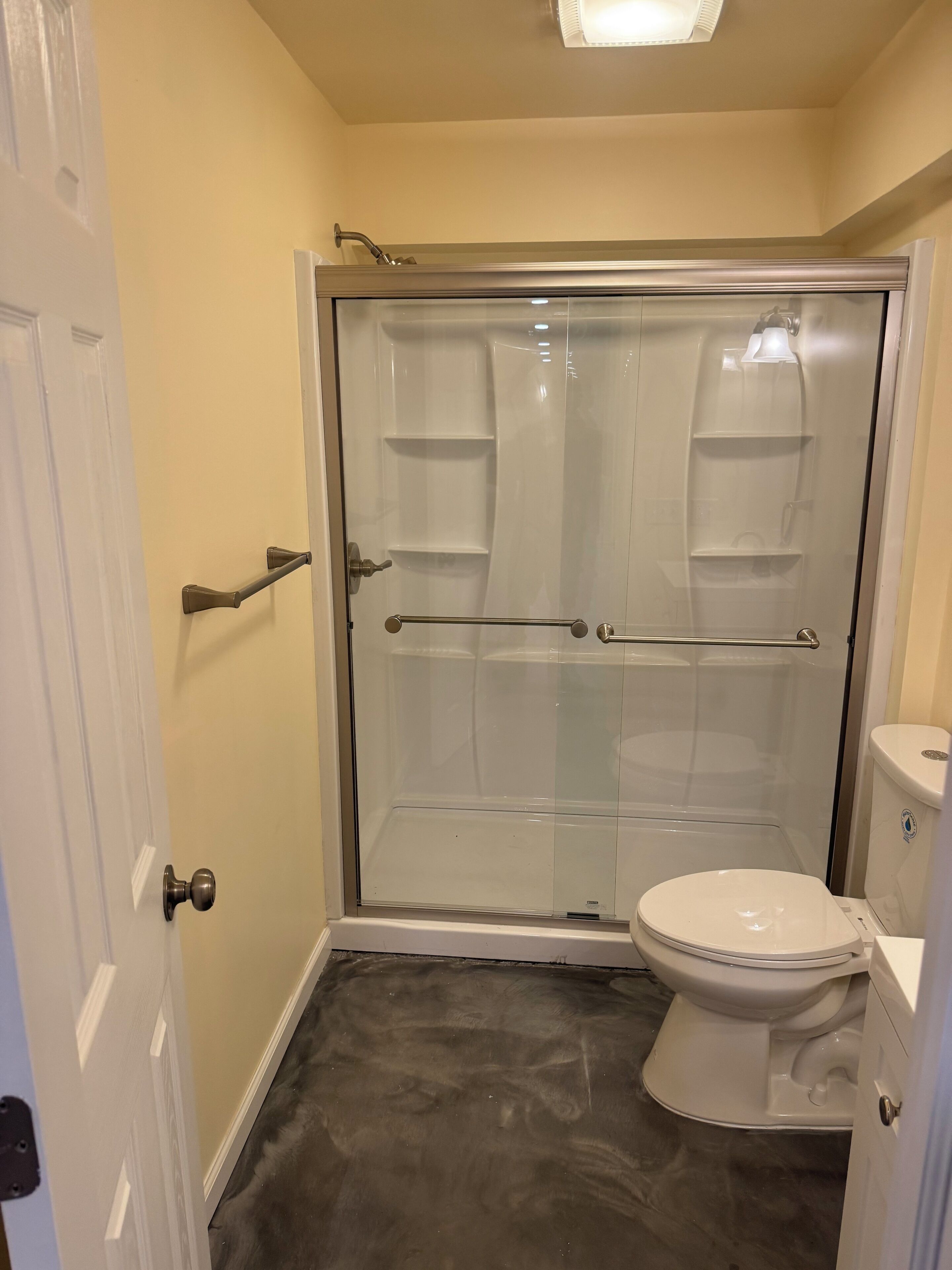 Een badkamer met een douchecabine van glas, een toilet en een deur met een handgreep.