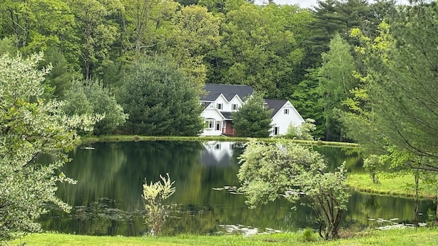 Una cabaña junto al lago con un muelle, rodeada de un bosque frondoso y un lago tranquilo.