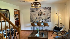 Un acogedor interior de cafetería con una mesa de madera, sillas de mimbre y un gran mural temático sobre café.