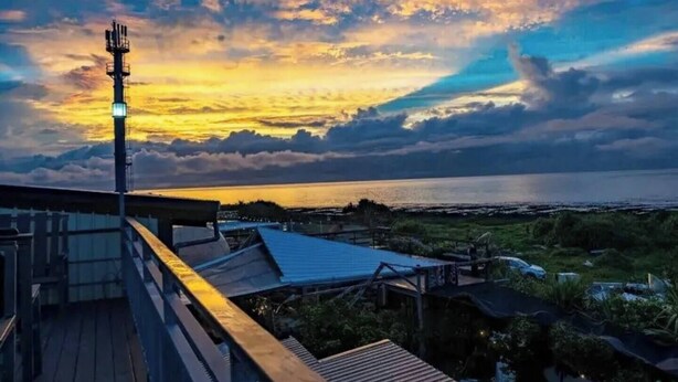A sunset view from a rooftop with a metal railing and a communication tower. - The Reef Diving Resort 海景雙人房b (Taitung County)